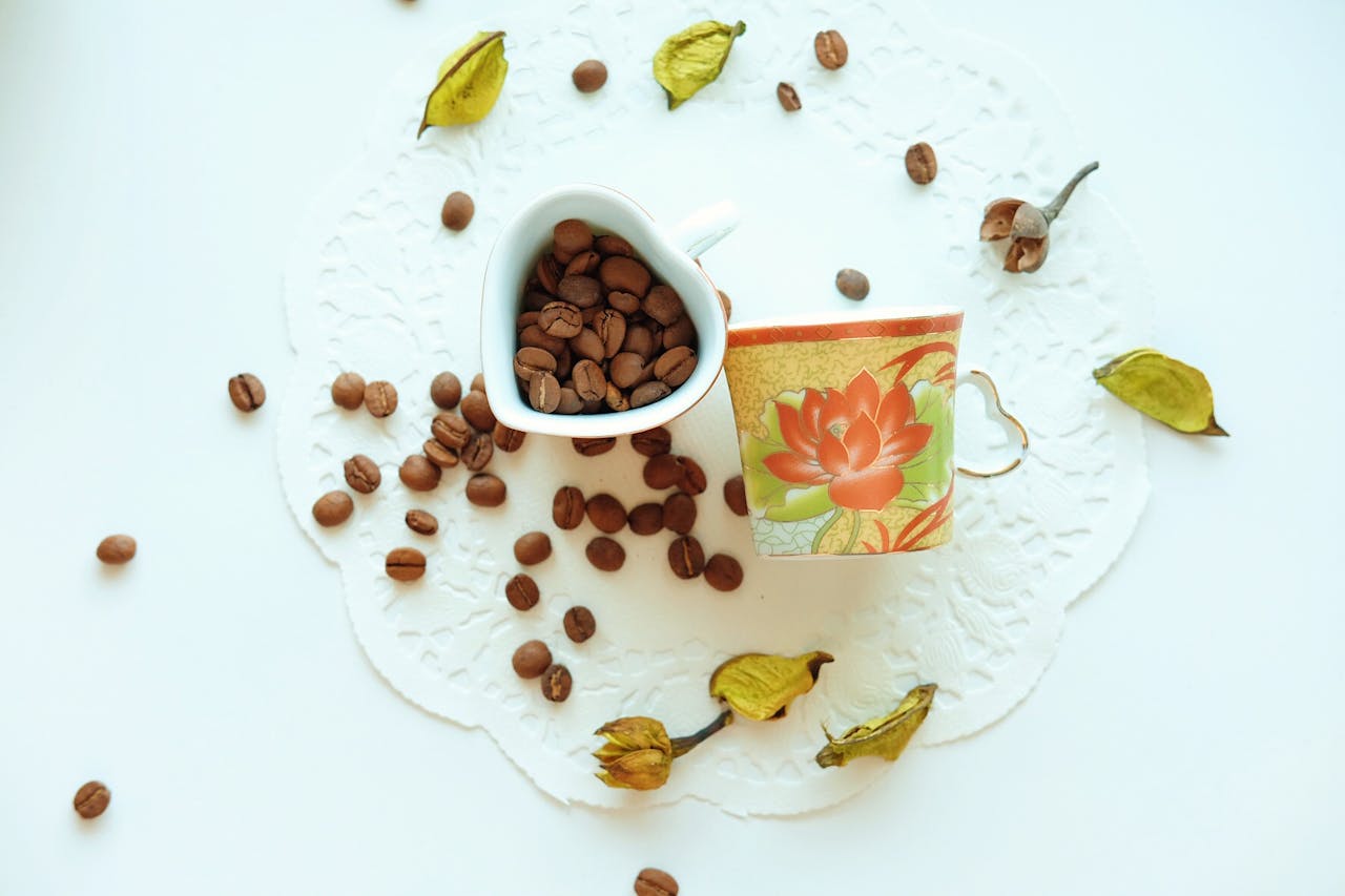 Flat lay of coffee beans and floral mug on delicate doily with artistic flair.